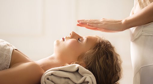 Mains d'une praticienne posées au-dessus du visage d'une femme allongée, séance de reiki